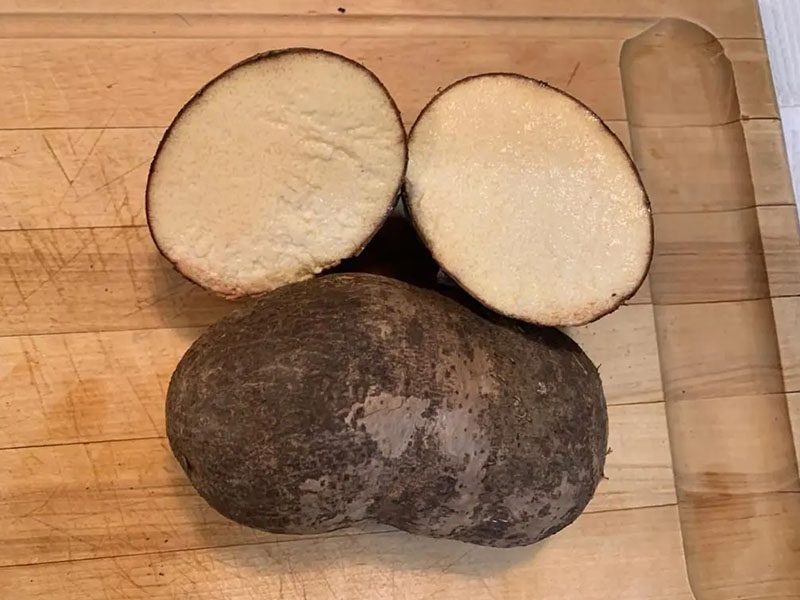 A brown potato cut in half on top of a wooden cutting board.